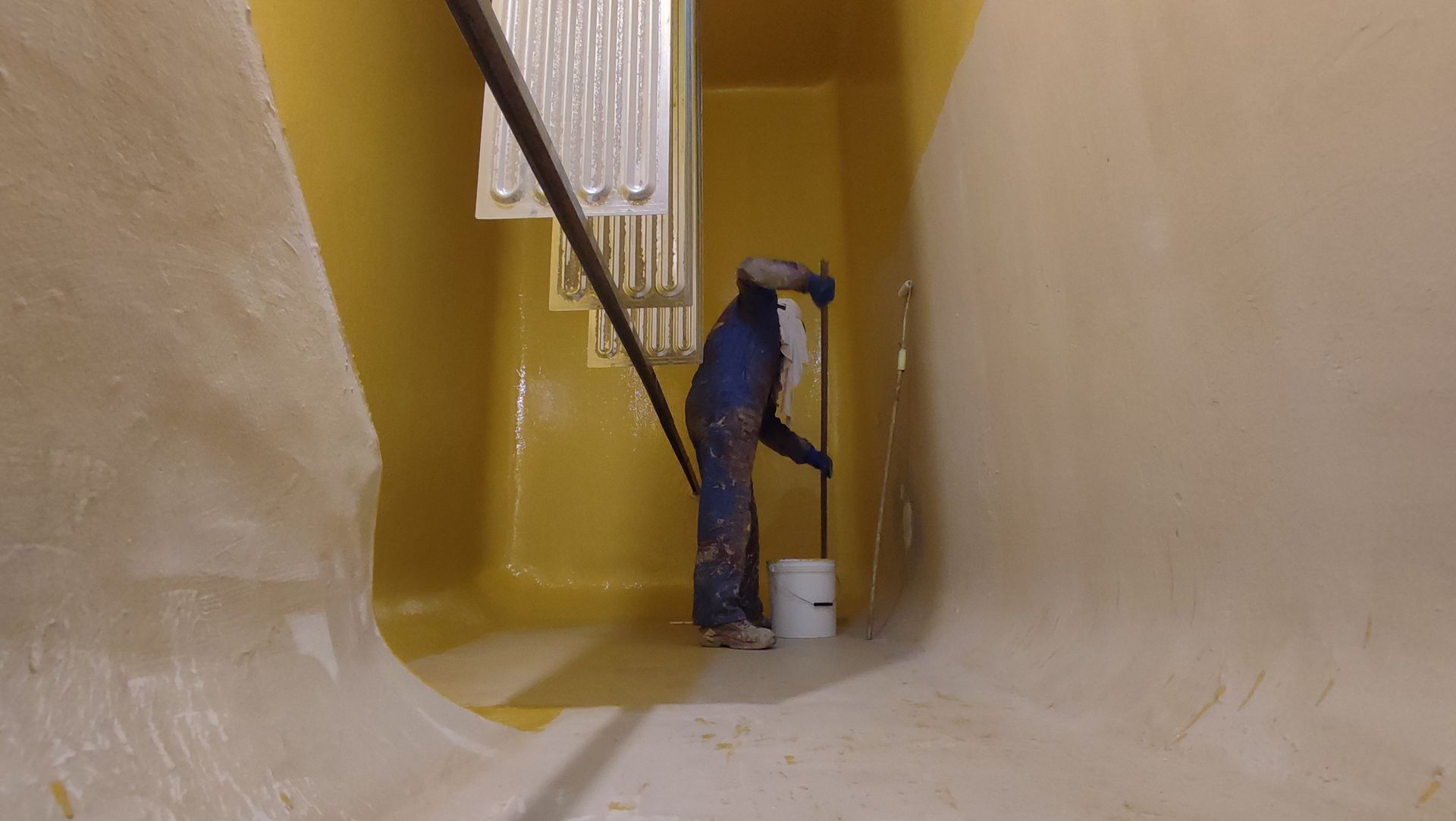 Una persona all'interno di una struttura dalle pareti gialle sta applicando della vernice bianca al muro con un rullo.