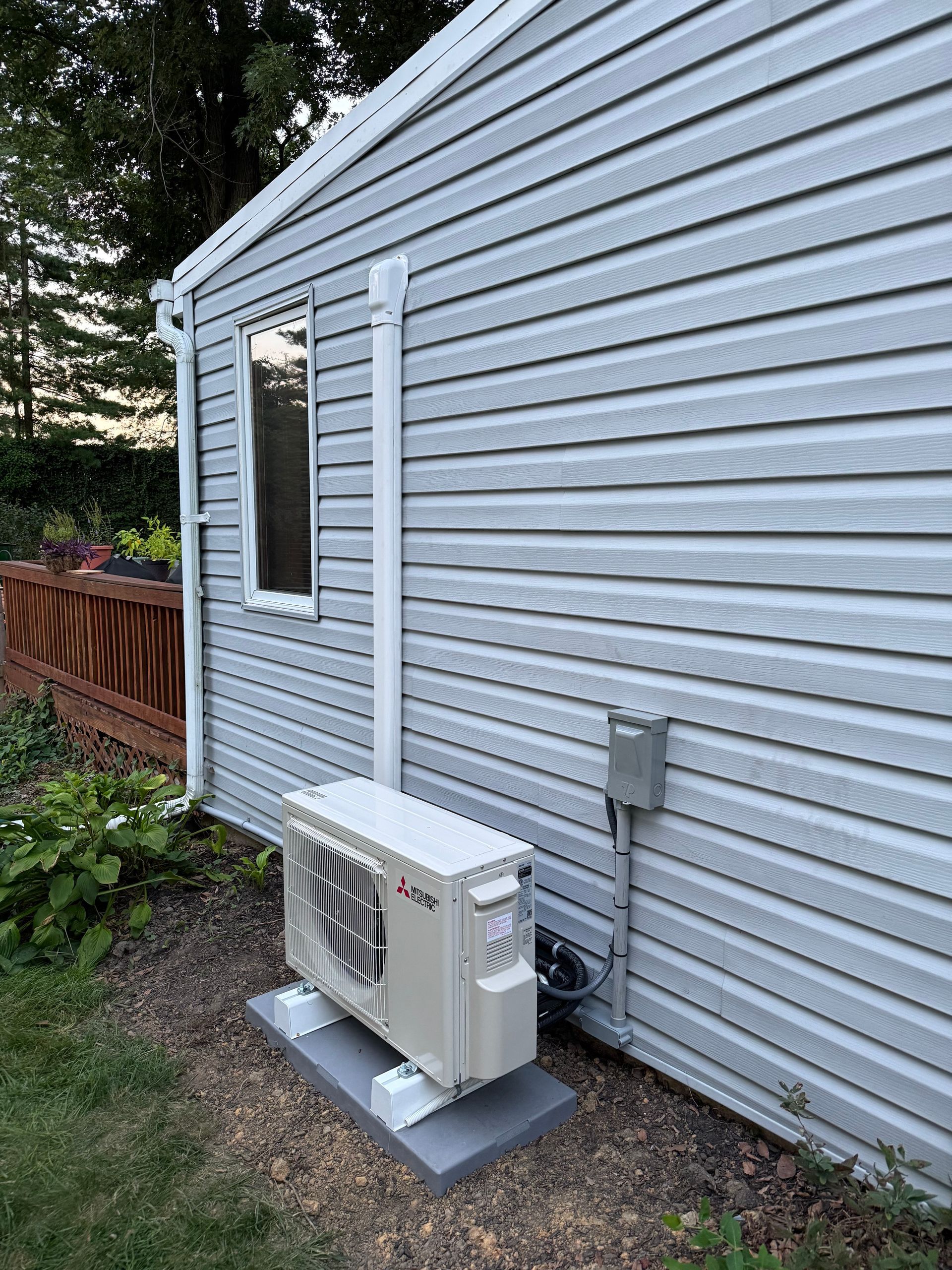 Mini-split heat pump unit installed outside a light gray siding building with a white exhaust pipe.