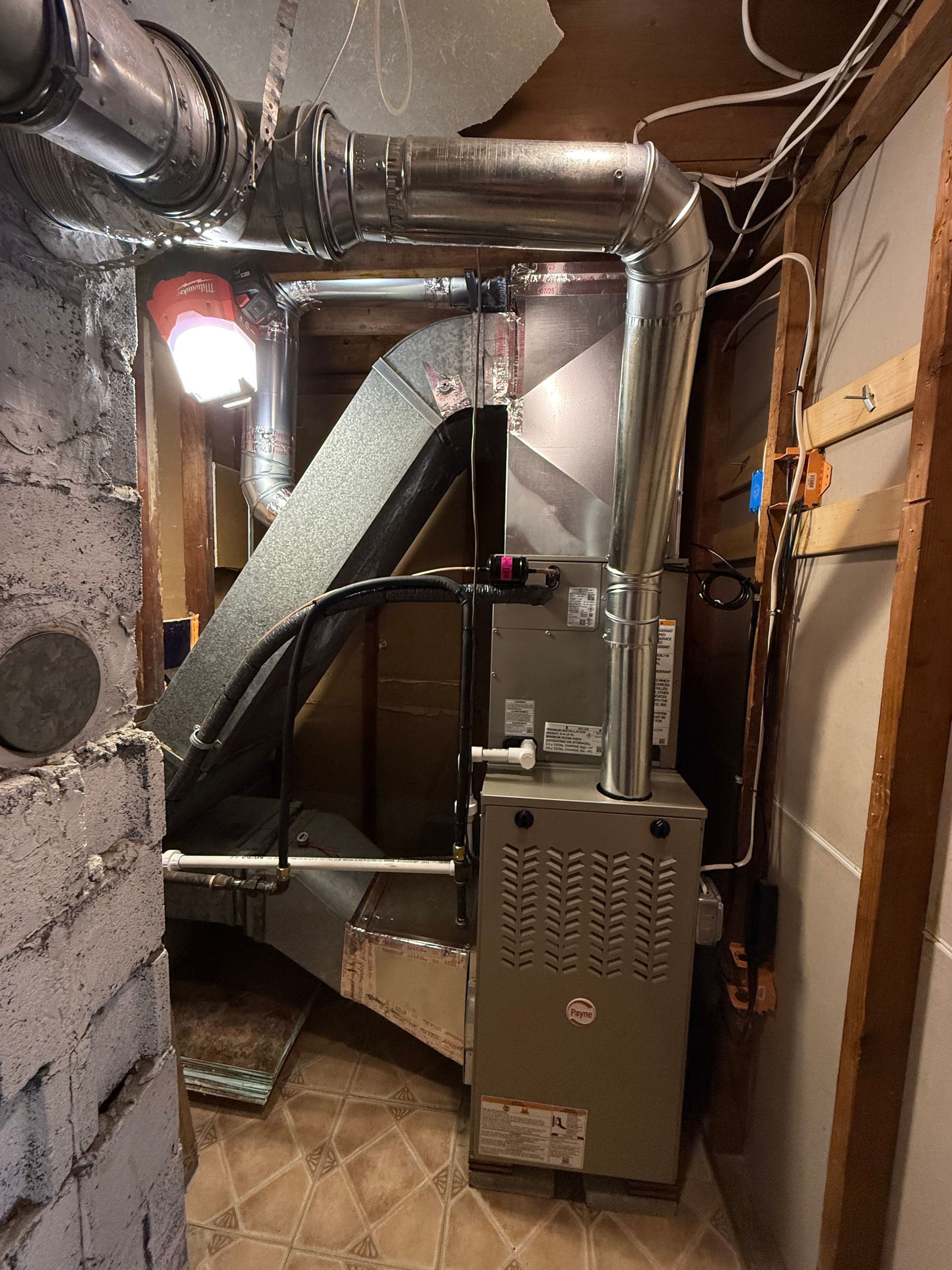 Furnace in a basement alcove with ductwork. Silver metal and gray colored components.