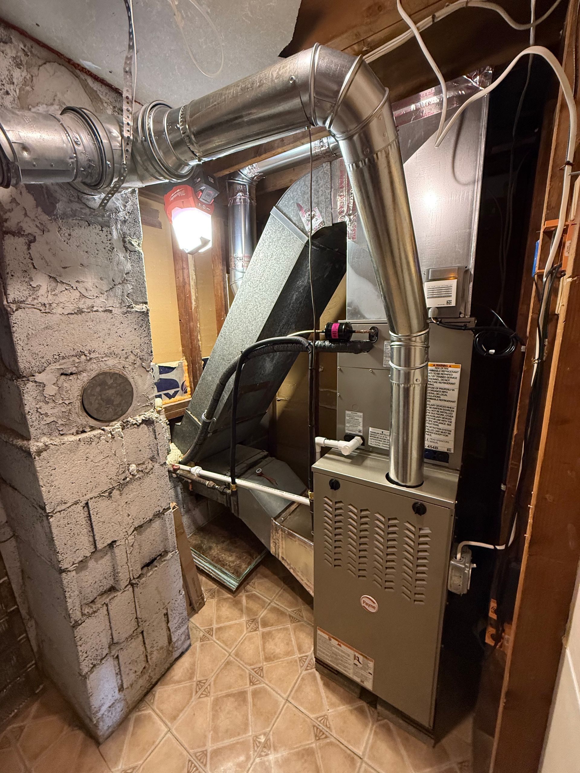 Furnace and ductwork in a utility room. Metal ducting connects to the furnace. Brick wall on the left.