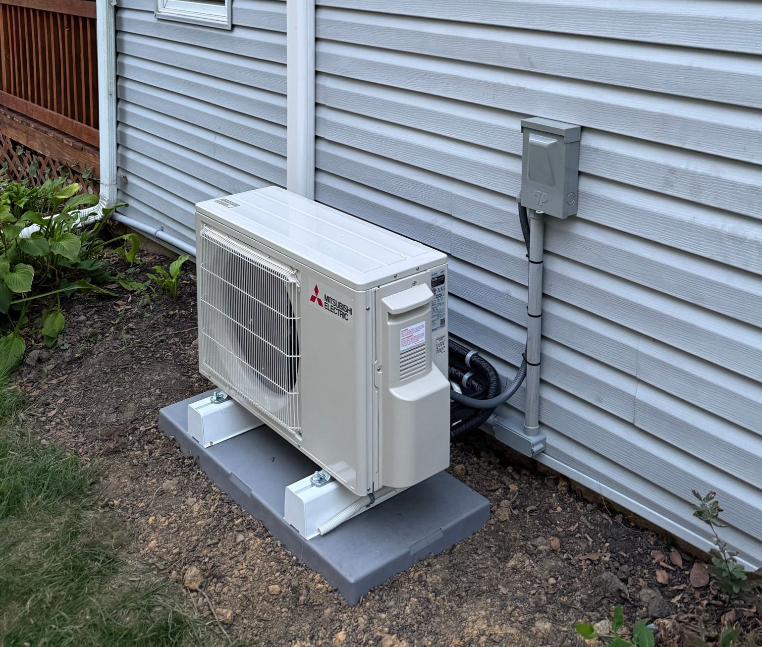 Mitsubishi heat pump unit outside a house, grey siding.