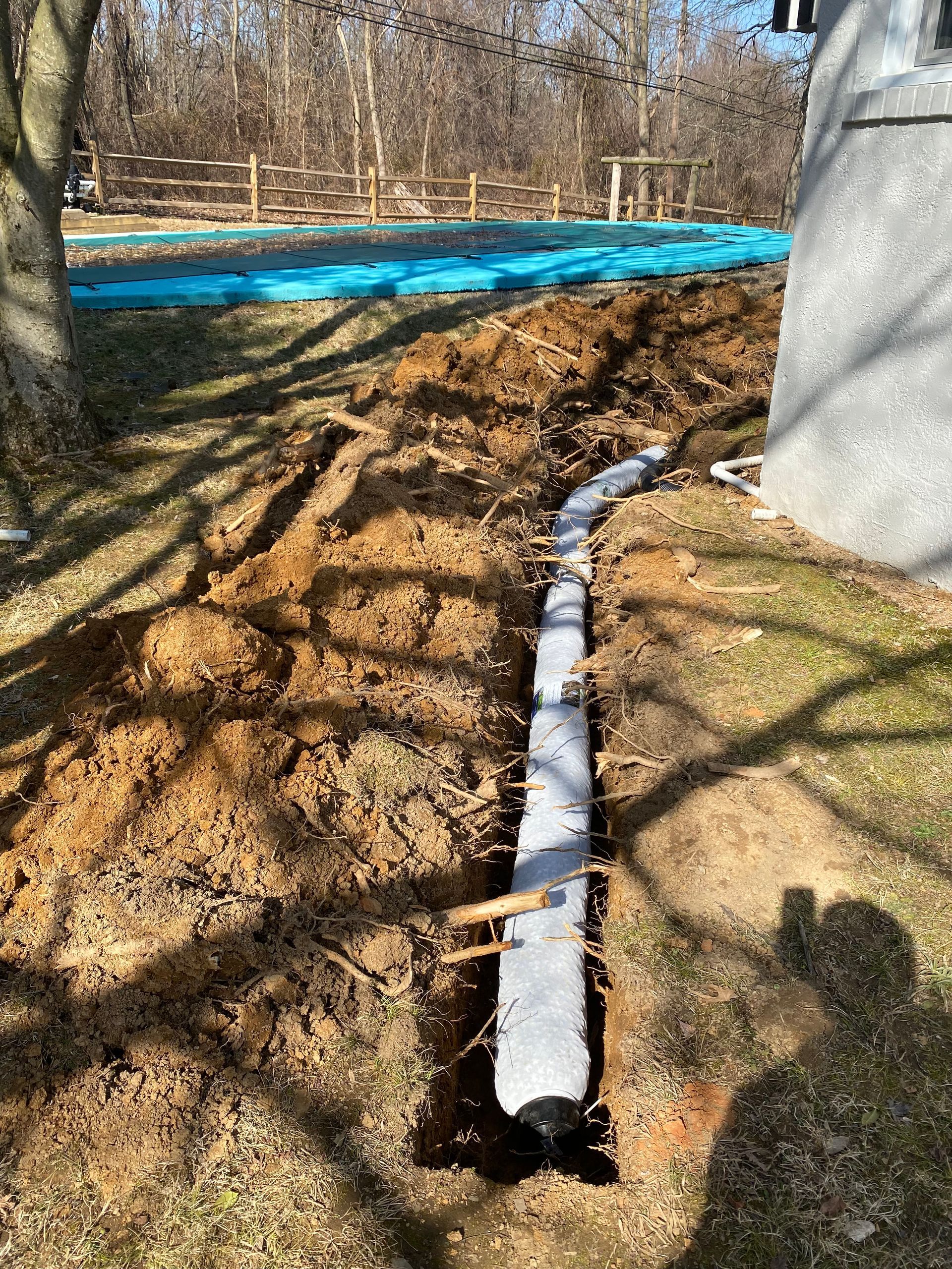 Trench dug beside a building, holding a concrete form. Lawn and trees surround the construction.