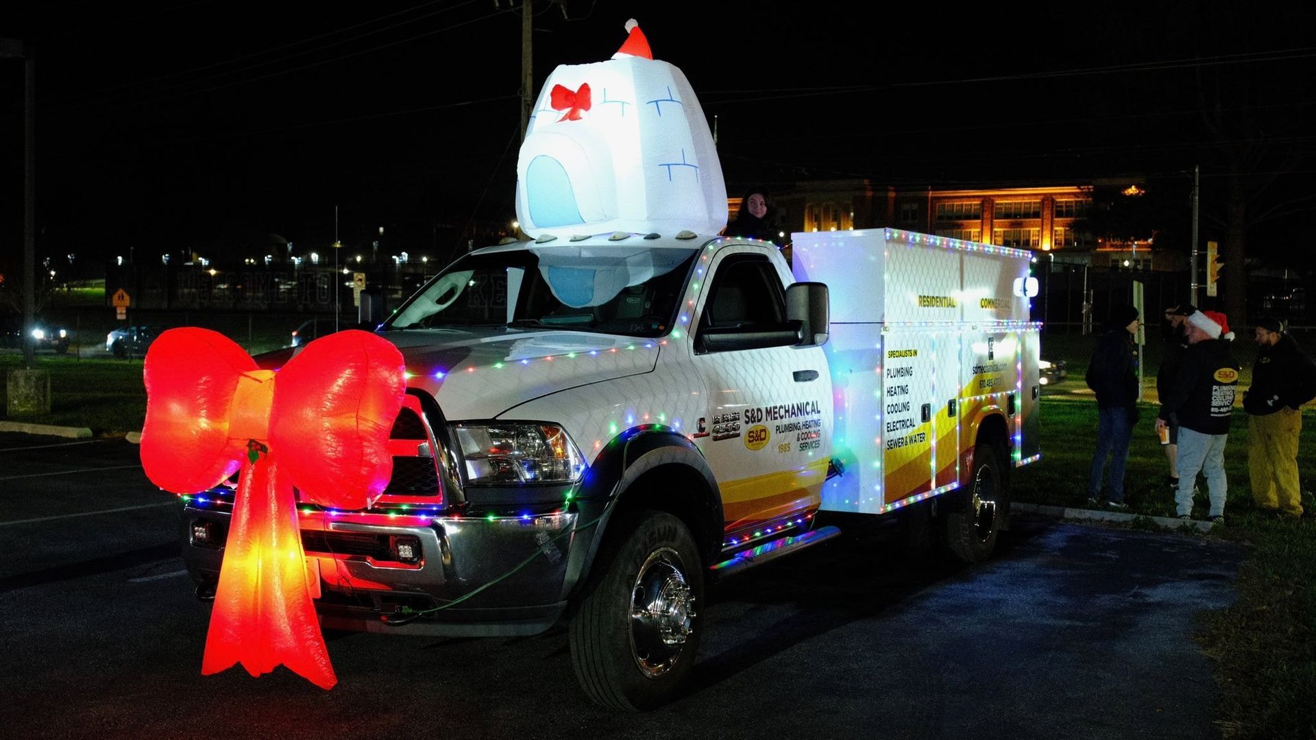 White truck decorated with lights and a large red bow, topped with an illuminated snowman.
