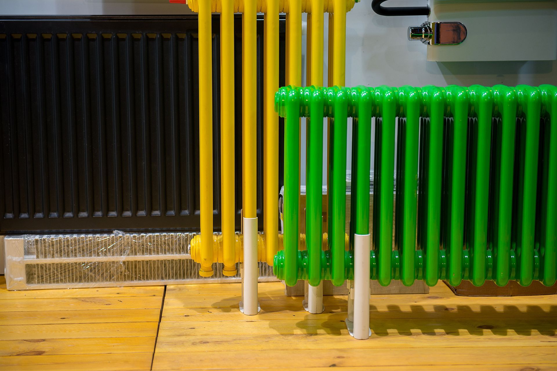 Radiators in various colors: black, yellow, and green, on a wood floor.