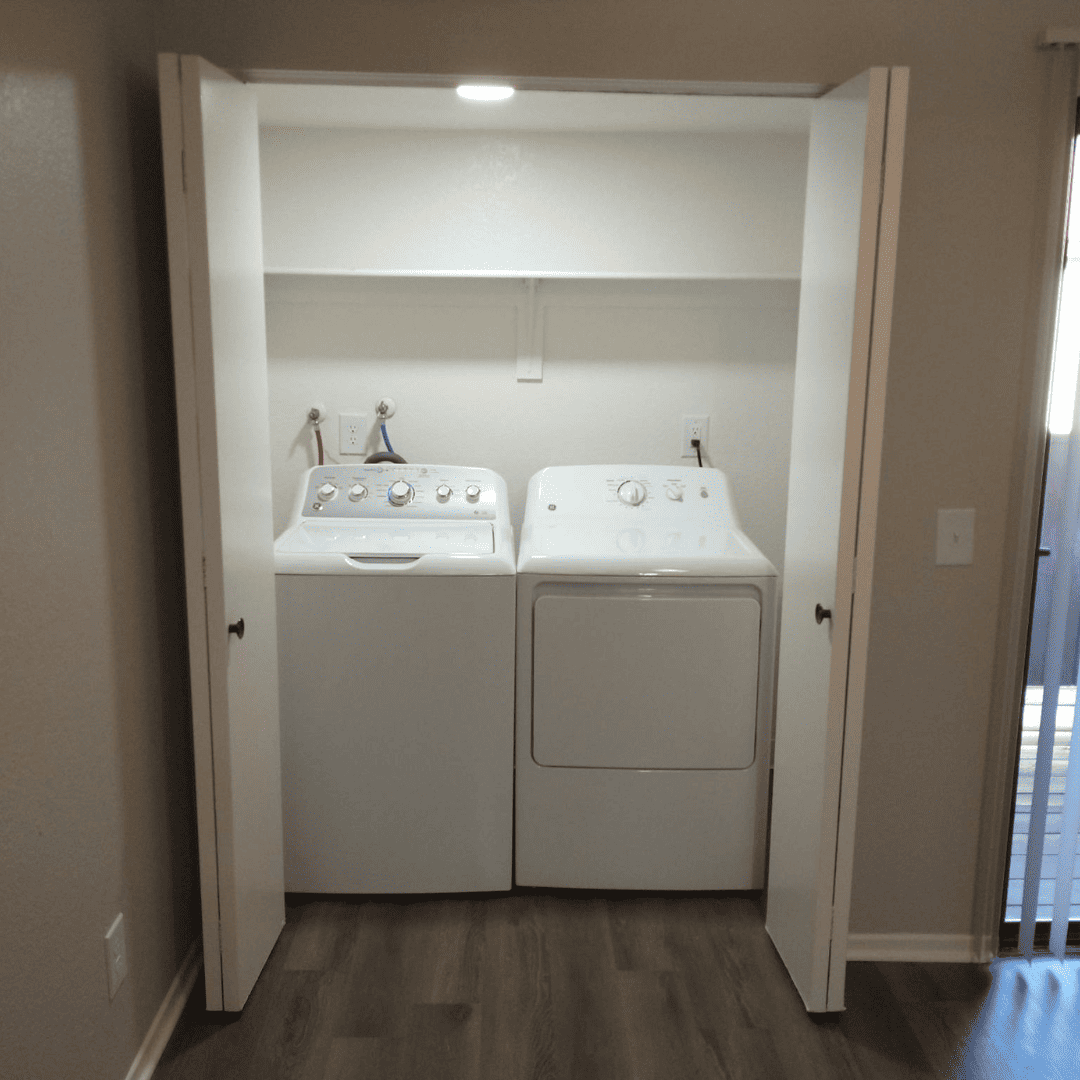 White washer and dryer inside a closet with open doors and a shelf above.