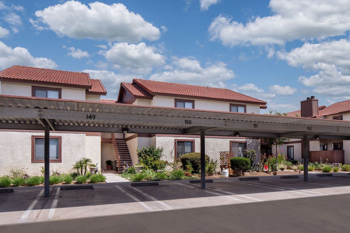 Apartment complex with tan stucco walls, brown trim, and red tile roof under a blue sky.