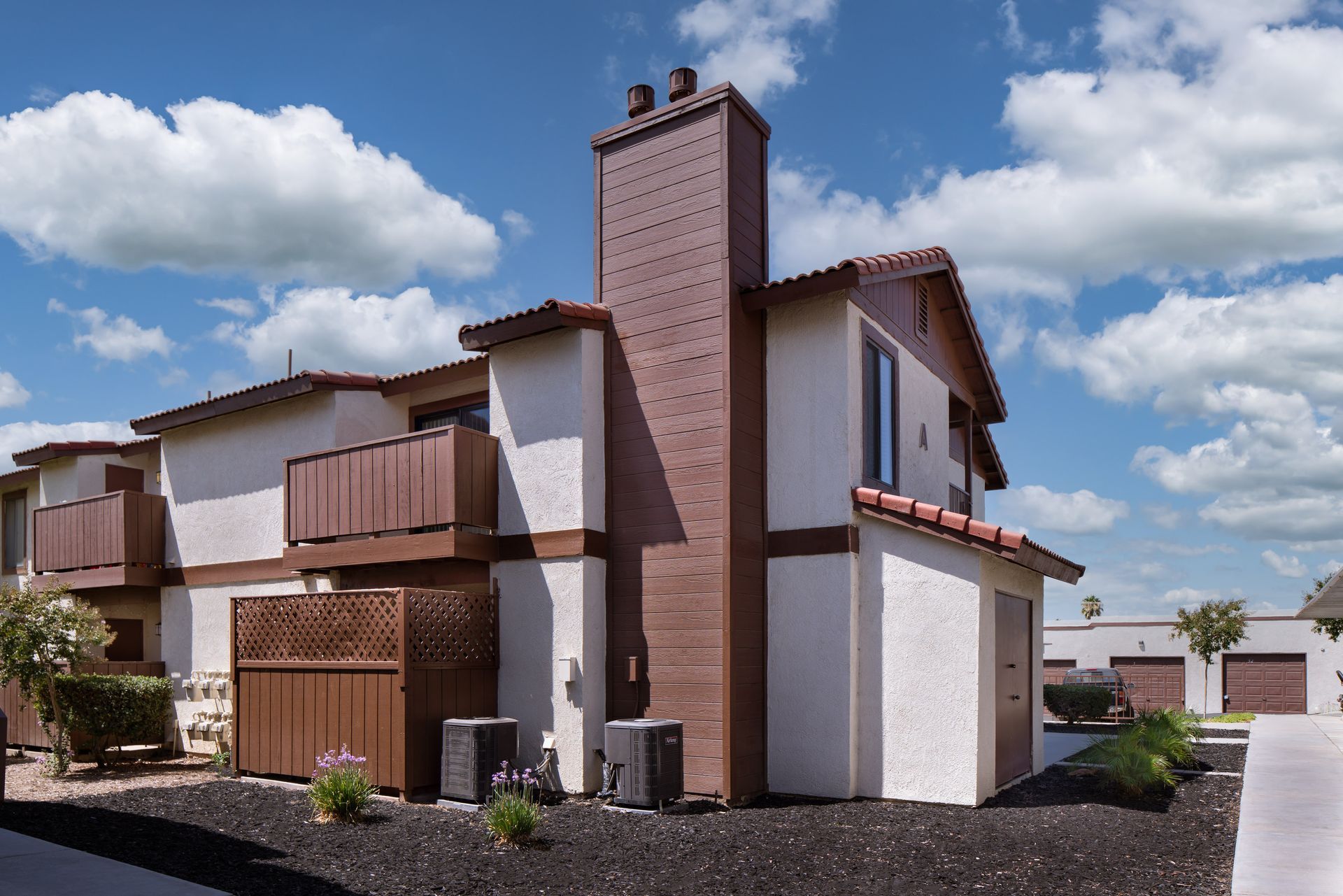 Apartment building with brown trim and a brick chimney under a blue sky with fluffy clouds.