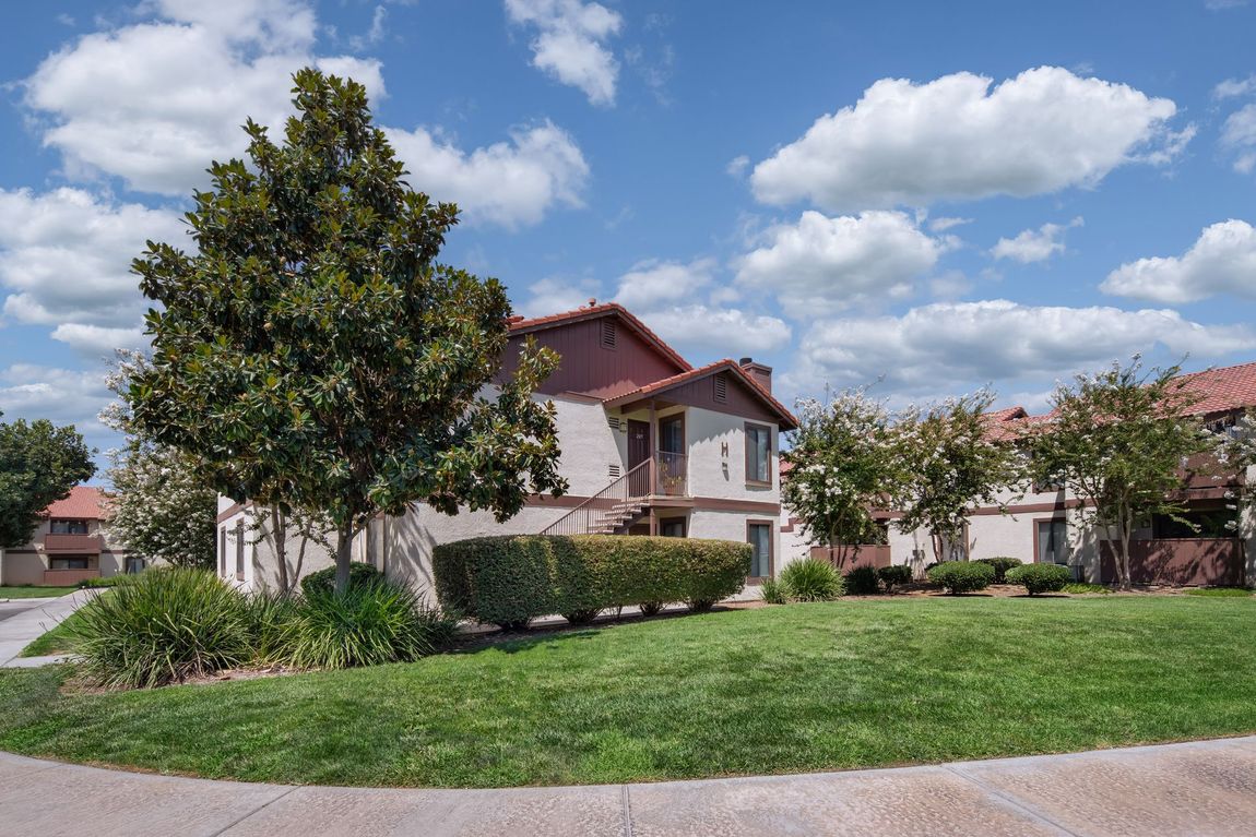 House with tan stucco, terracotta roof, and green lawn under a partly cloudy sky.