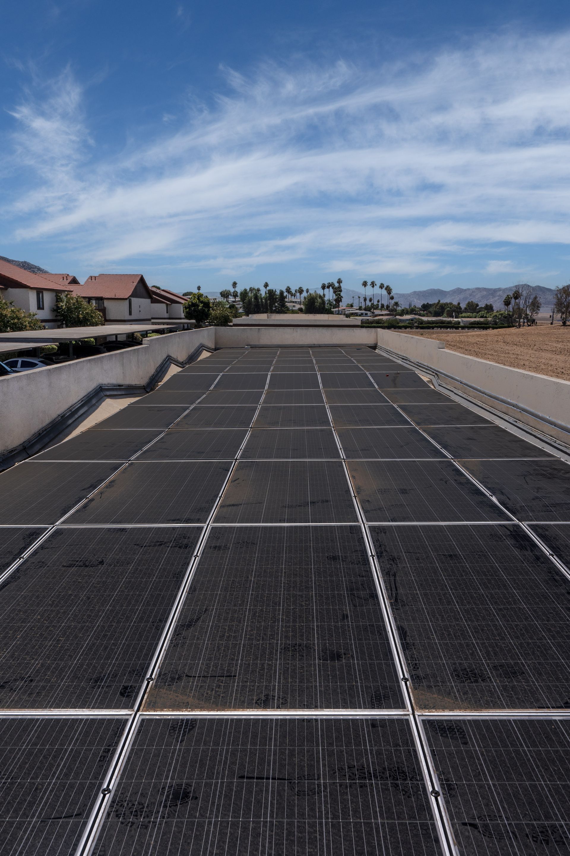 Solar panels on a flat roof, with houses and blue sky in the background.