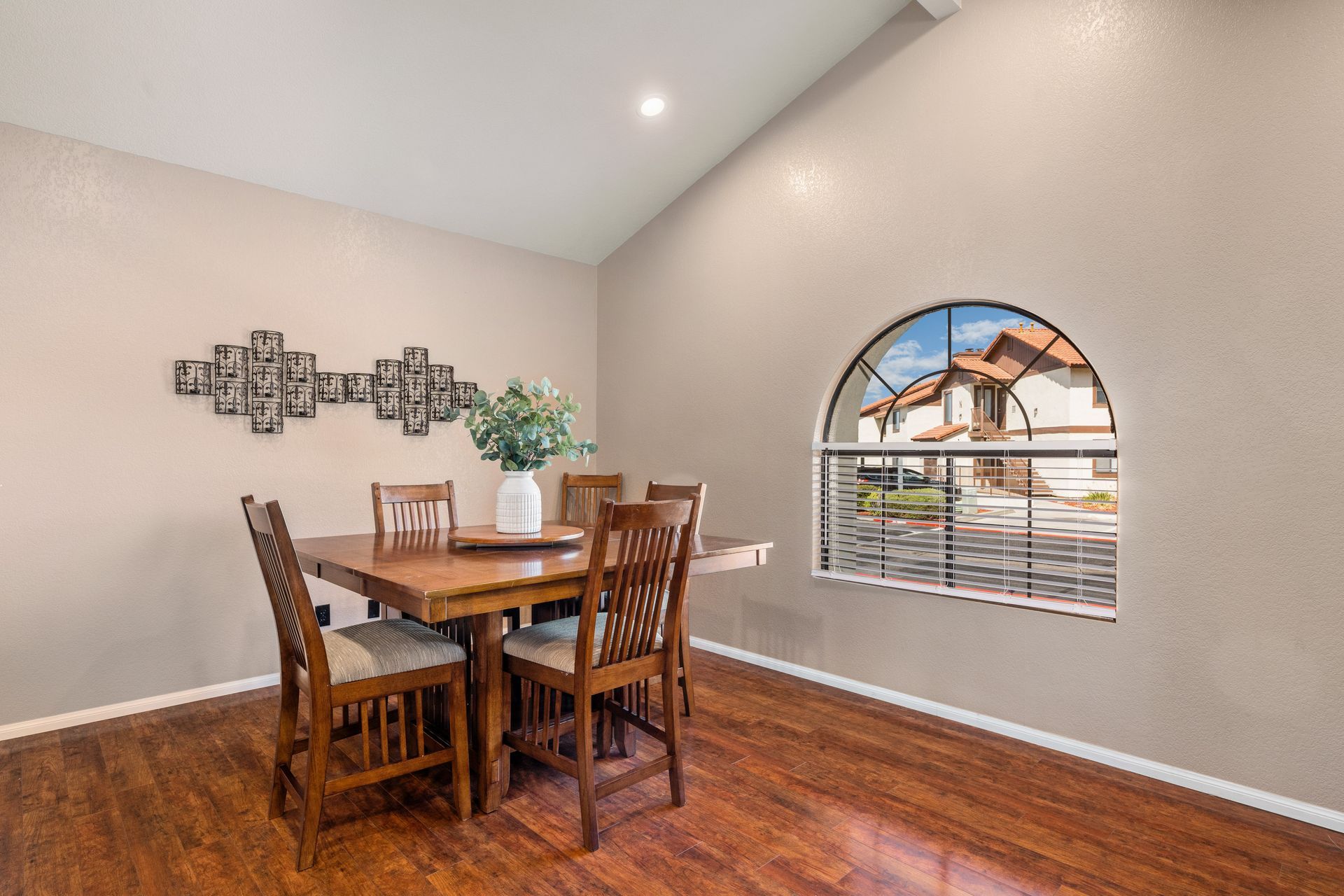 Dining room with wooden table, chairs, arch window overlooking a neighborhood, and wall decor.