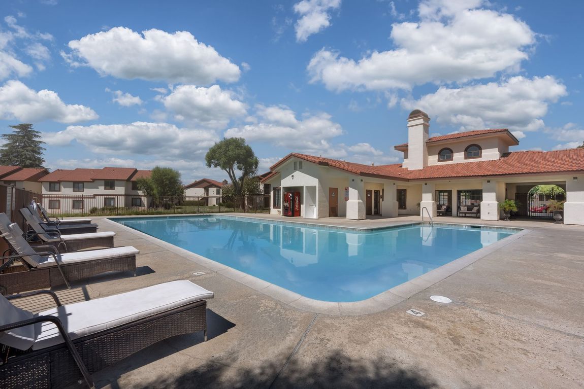 Swimming pool with lounge chairs and a clubhouse under a blue sky with clouds.