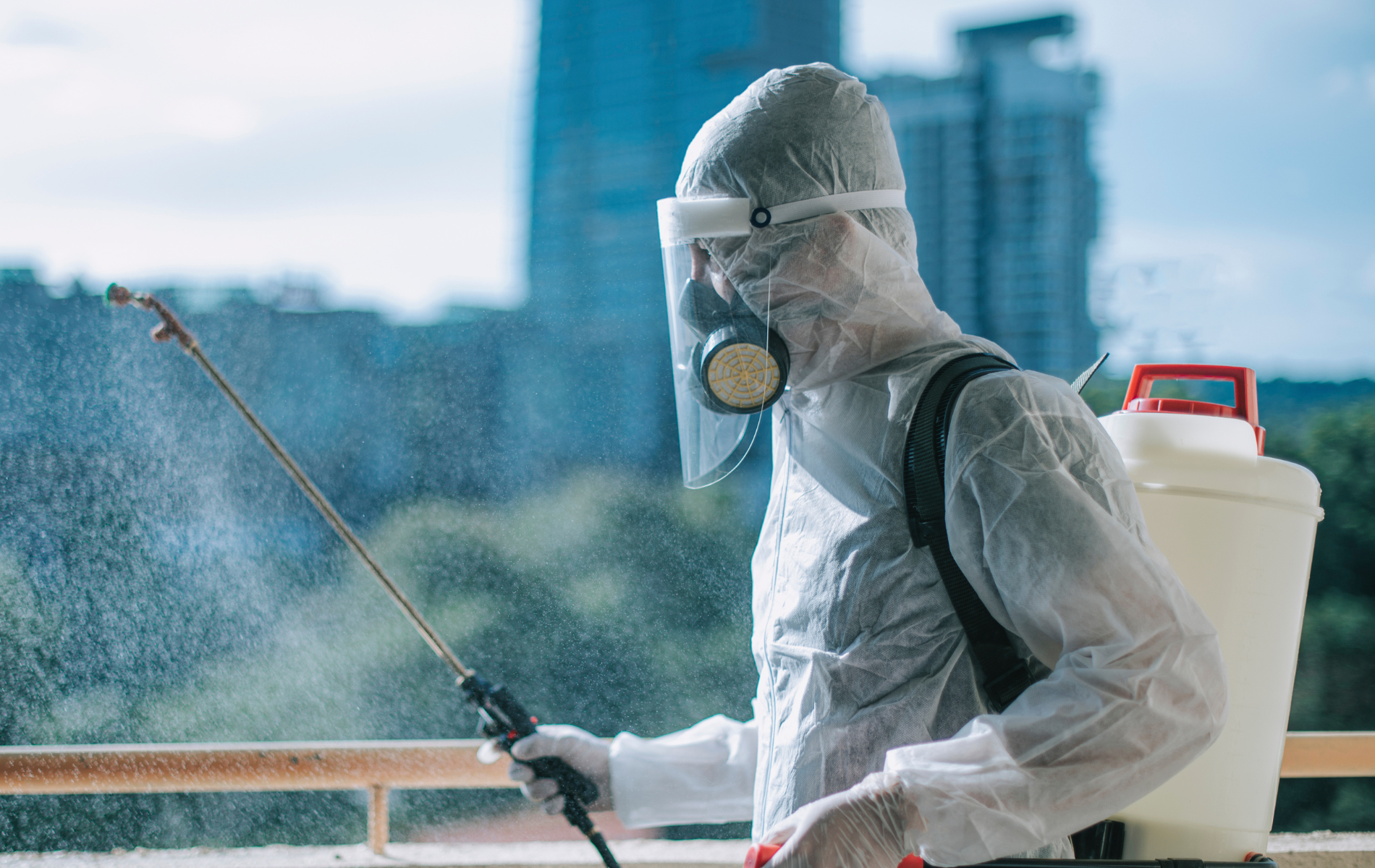 Person in hazmat suit spraying disinfectant outside.