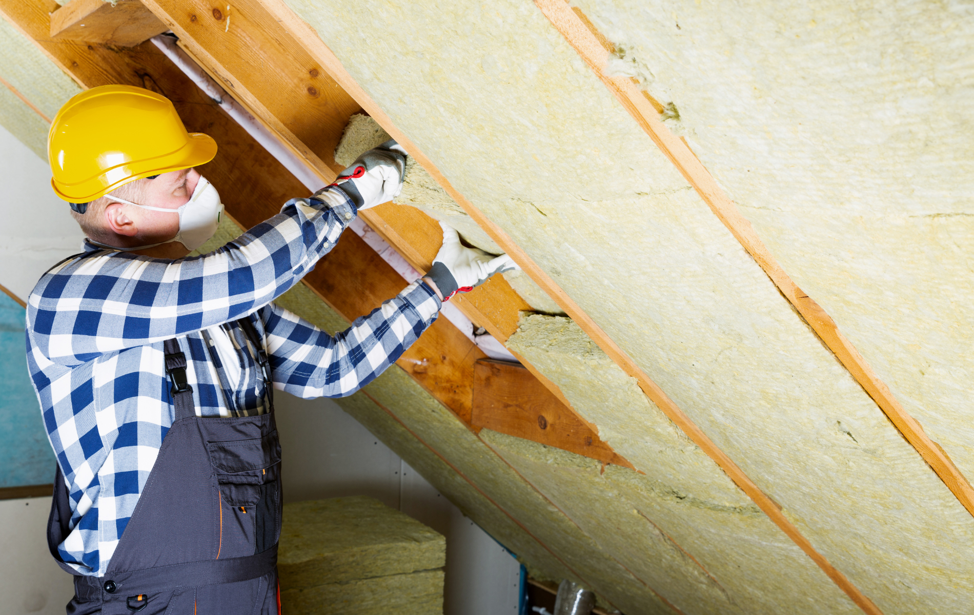 Worker in yellow hard hat installing insulation in attic.