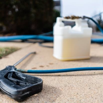 A pressure washer is sitting on the ground next to a hose and a bottle of liquid.