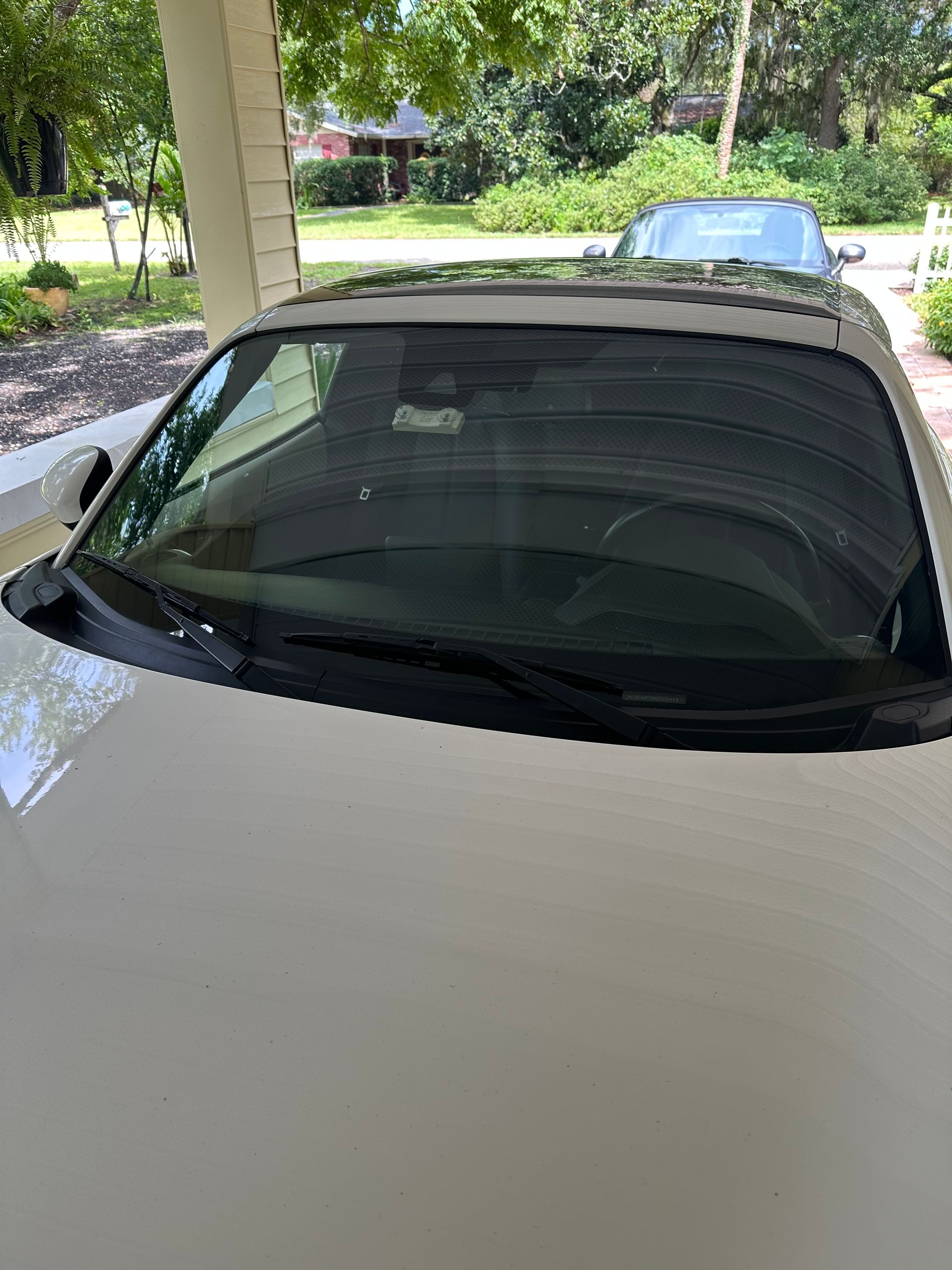 White car with sunroof parked under a covered area, with a second car visible in the background.