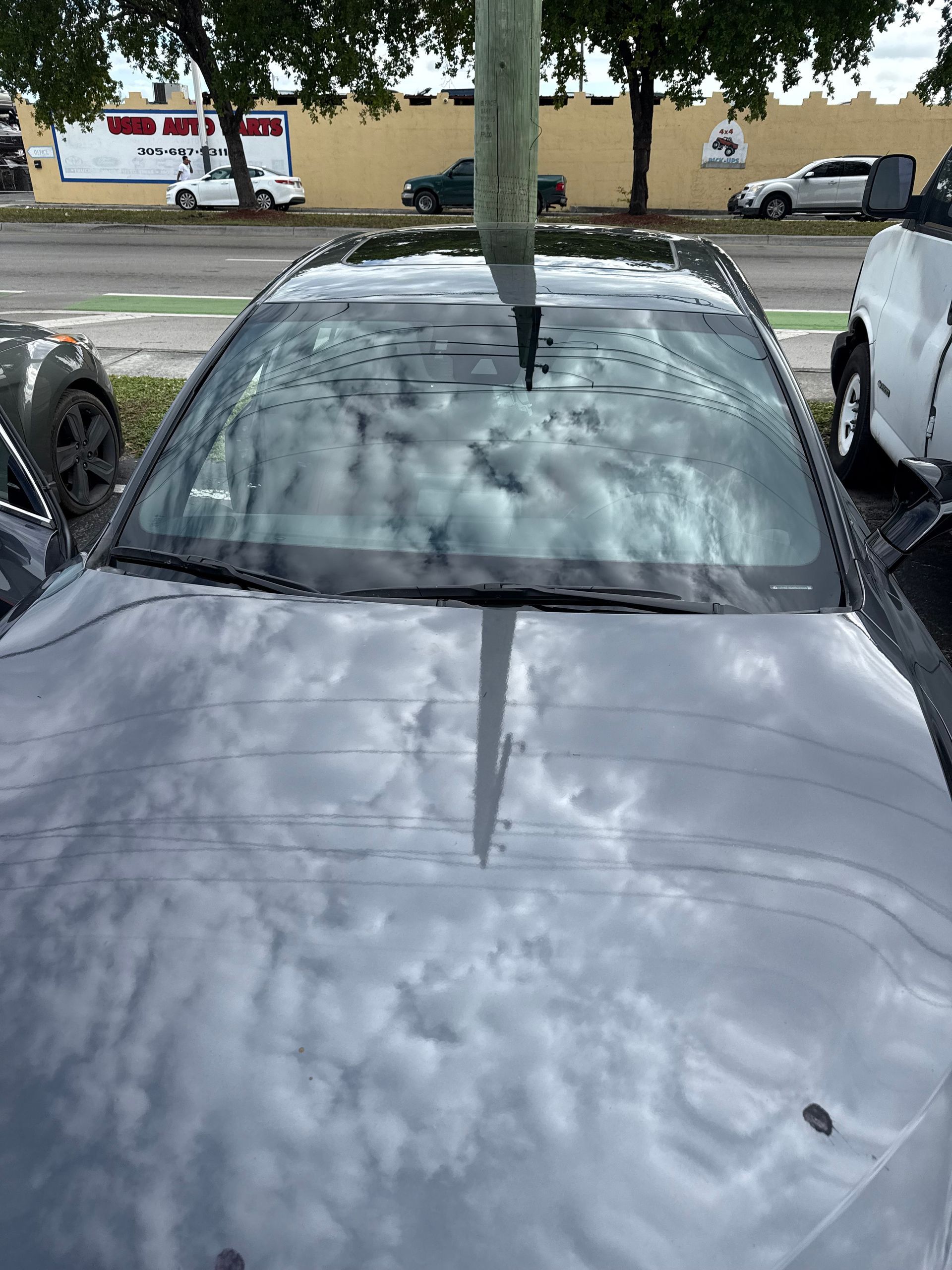 A dark car with rain drops on the windshield, parked outside. A pole is centered.