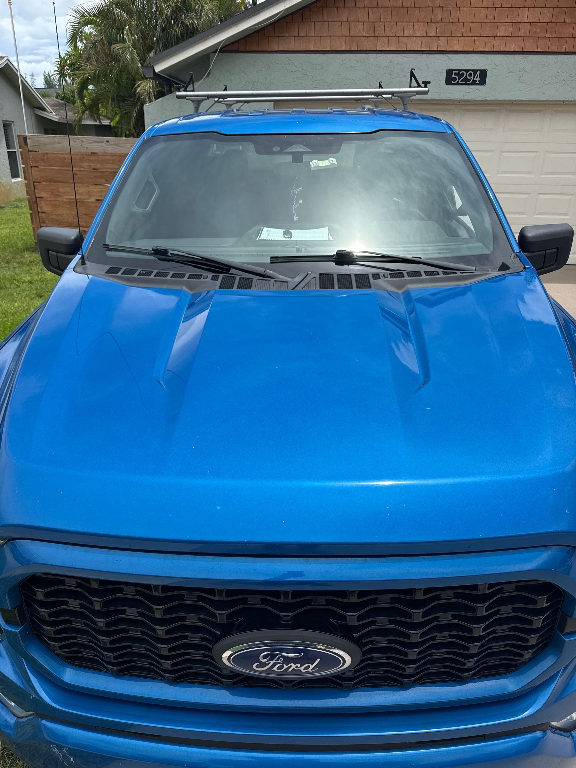 Blue Ford truck with black grill and roof rack, parked in front of a building.