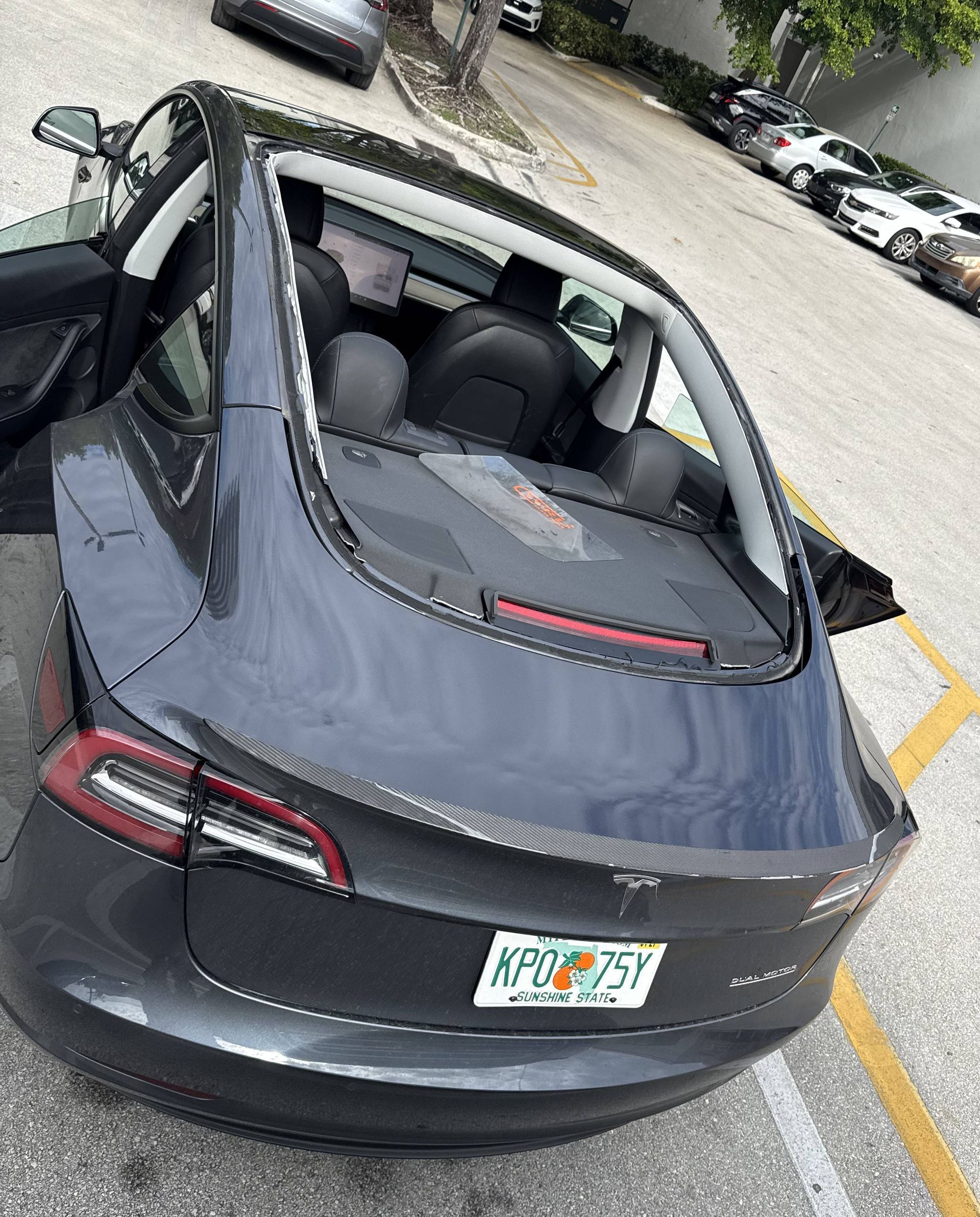 Dark gray Tesla Model 3 with open trunk in a parking lot.