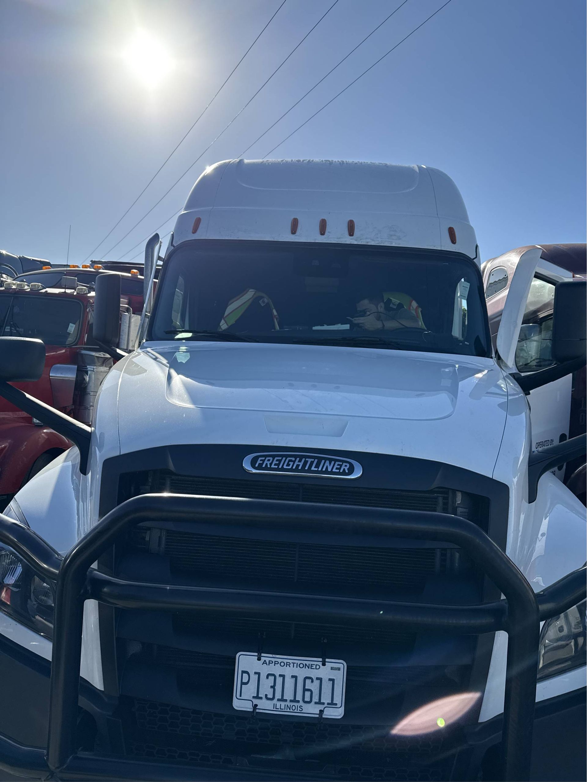 White semi-truck with a black grill guard, parked in a sunny lot, California license plate.