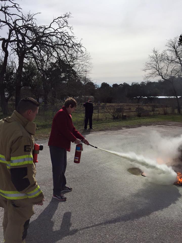 A fireman is teaching a woman about how to use a fire extinguisher to put out a fire.