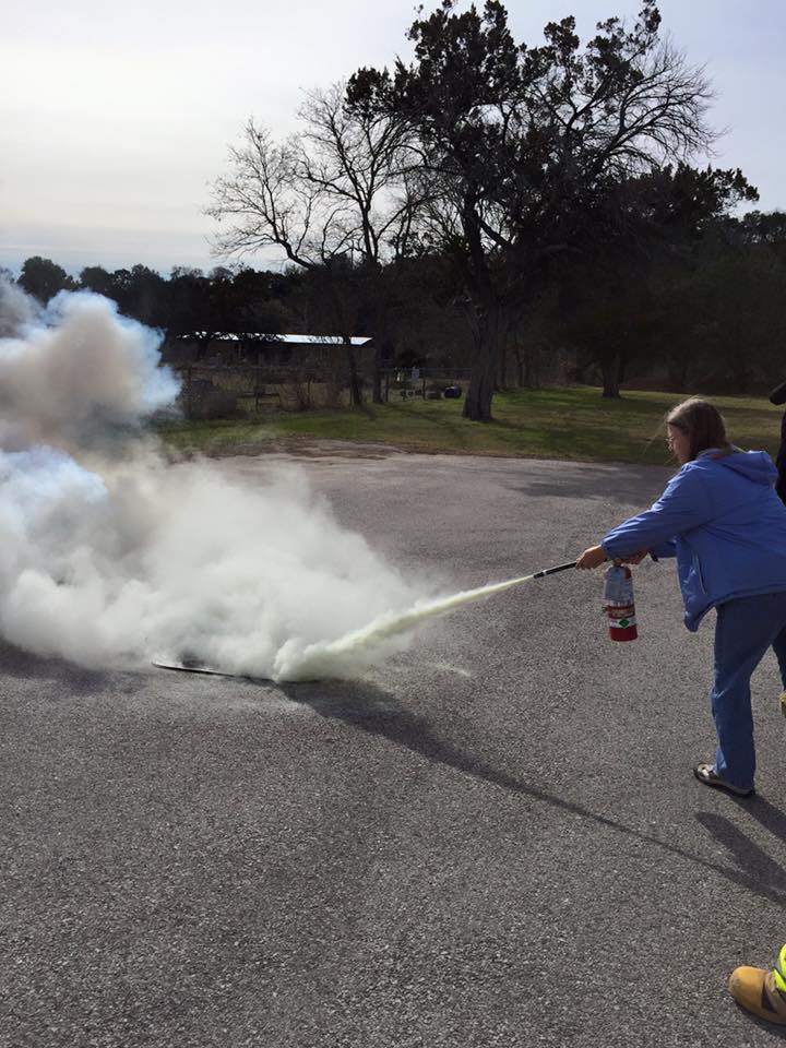 A woman is practicing using a fire extinguisher.