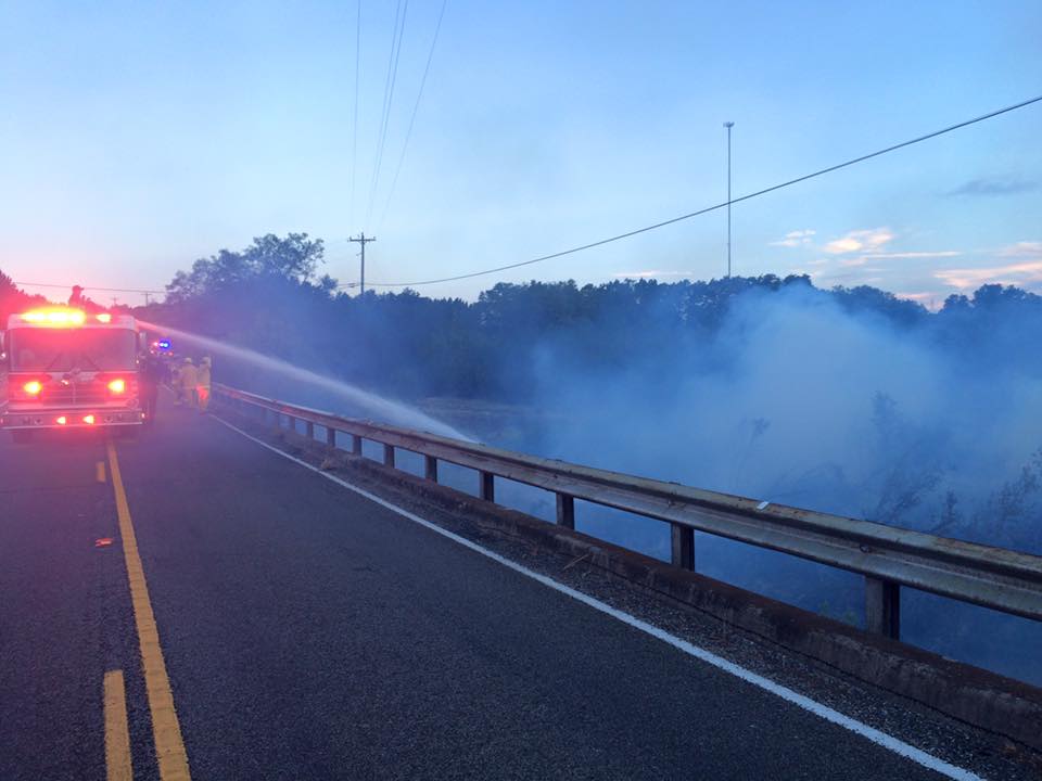 A fire truck is spraying water on a fire on the side of a highway.