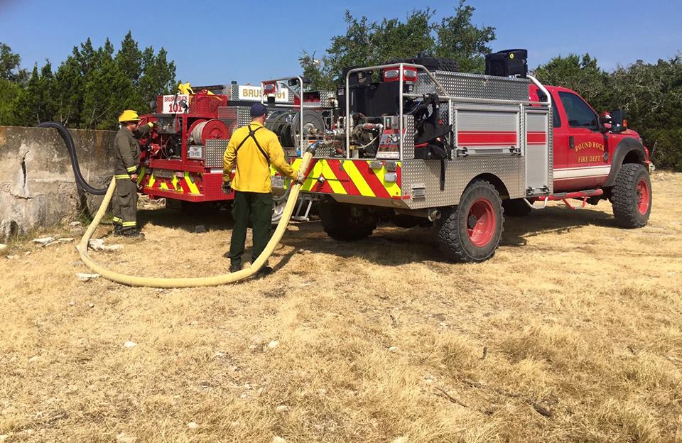 Two firefighters are pumping water from a hose to a fire truck.
