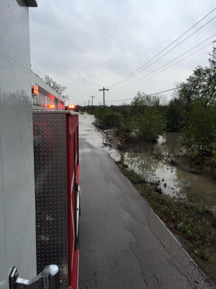 A fire truck is blocking a flooded road next to a river.