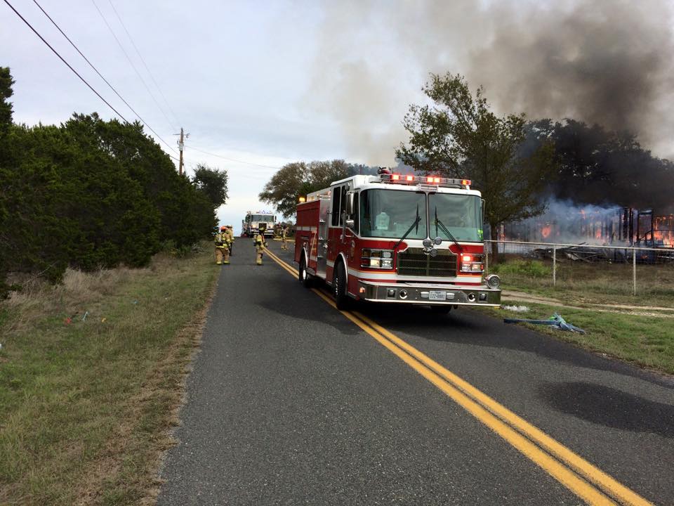 A fire truck is parked on the side of the road near a fire