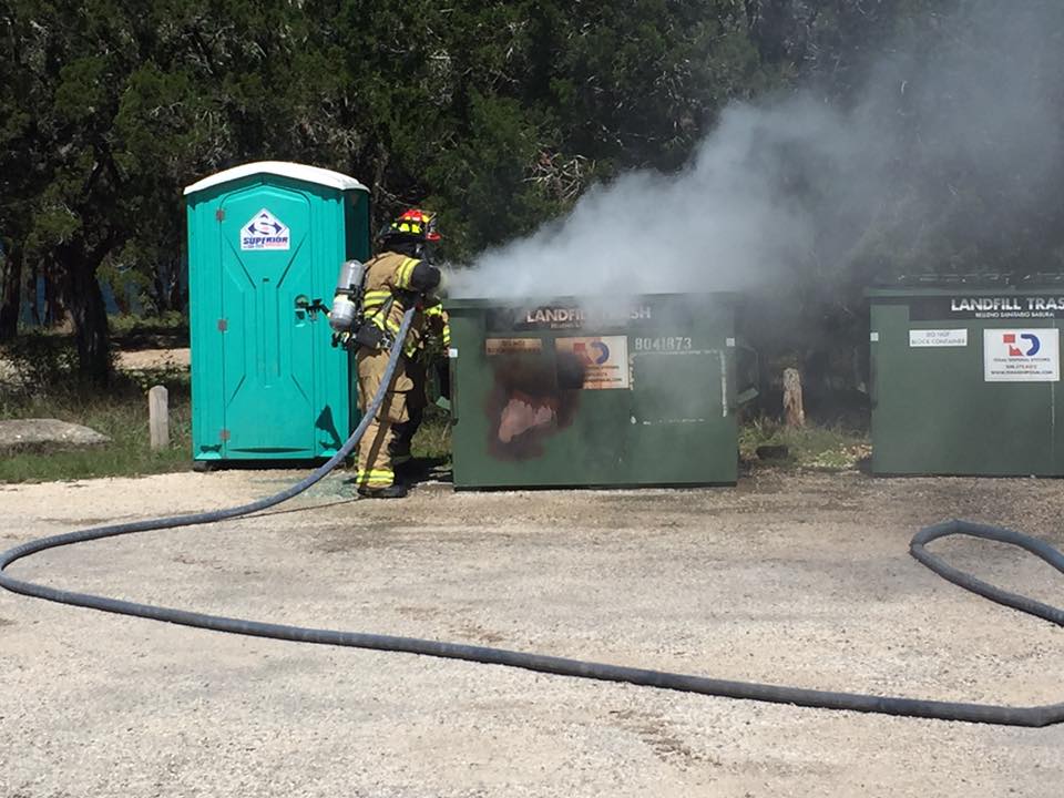A fireman is using a hose to extinguish a fire in a dumpster.