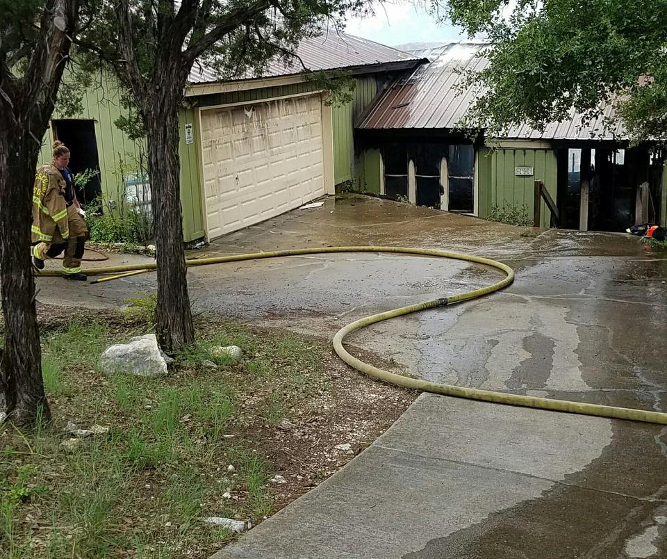 A fireman is standing in front of a house with a hose in the driveway.