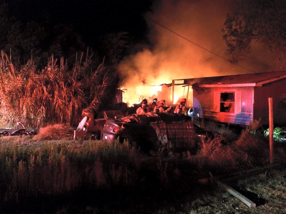 A group of fire fighters are working on putting out a mobile home that is on fire.