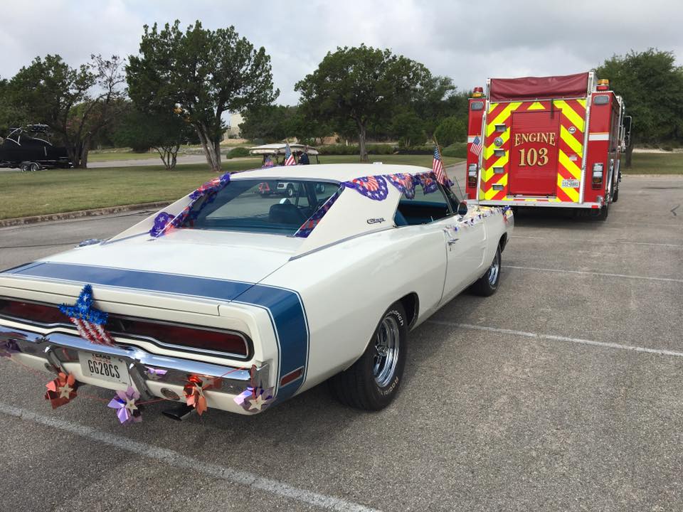 A white car is parked behind a red fire truck for a parade.