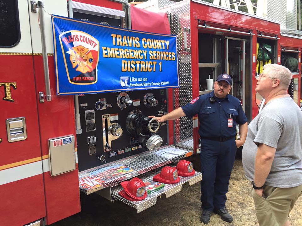 Two men are standing in front of a fire truck with a sign that says travis county emergency services district 1