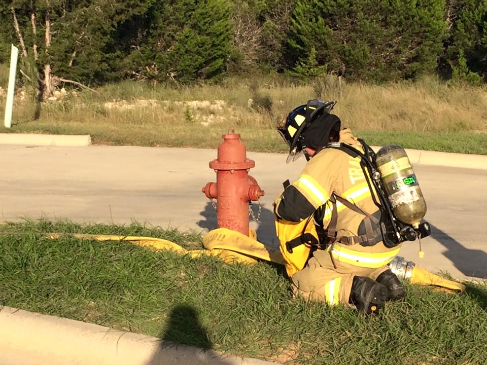 A firefighter is kneeling down next to a fire hydrant.