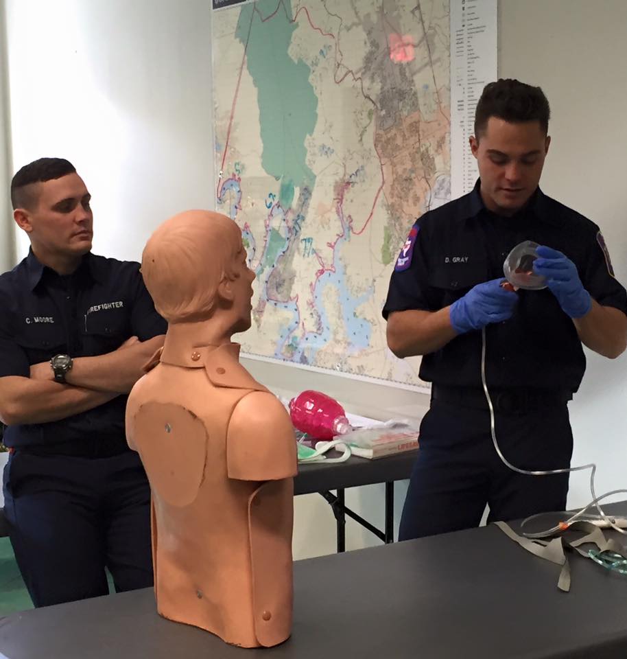 Two EMS personnel standing next to a mannequin and a map