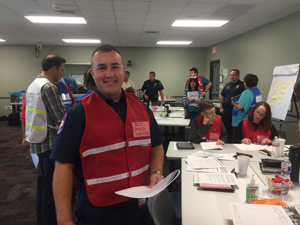 A man in a red vest is standing in front of a group of people.