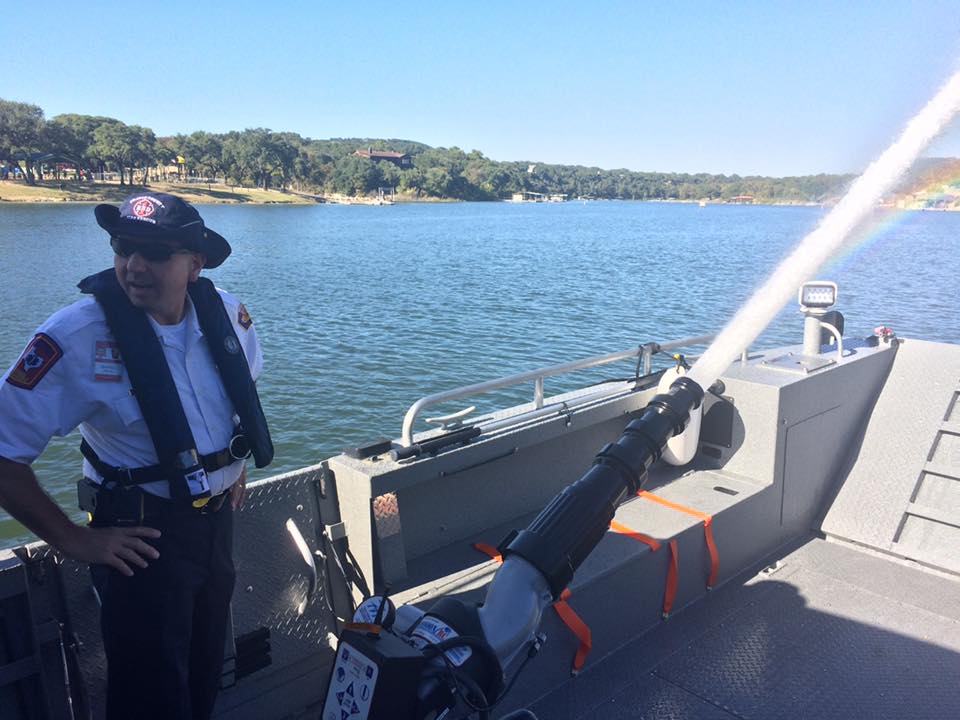 A man in a life jacket is standing on a boat near a body of water.