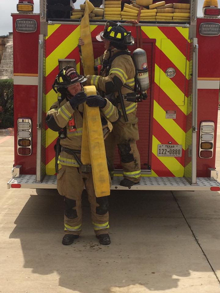 Two firefighters holding a yellow hose at the back of a fire truck