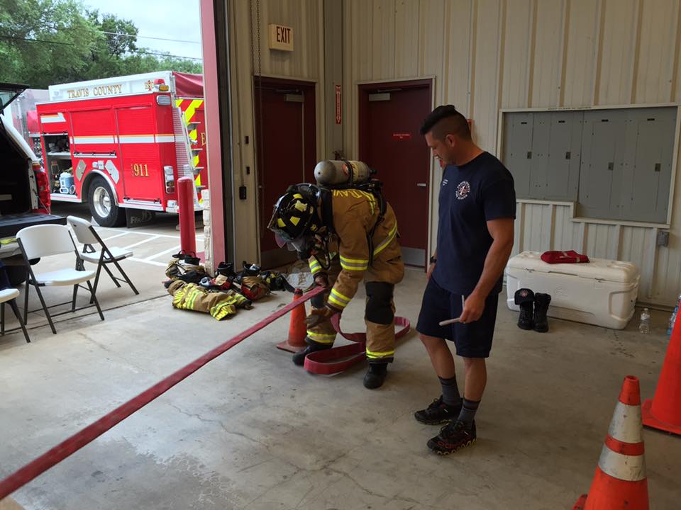 A fireman is standing next to another fireman in a garage  during a physical agility test.