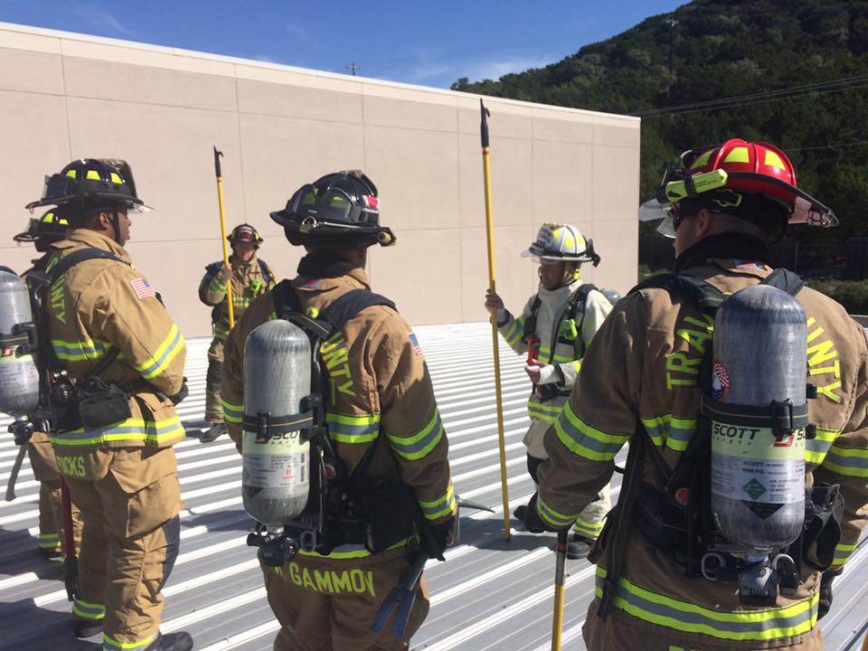 A group of fire fighters are standing while listening to an instructor during a training exercise.