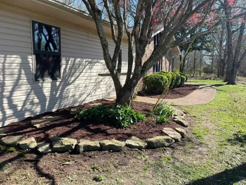 A home's exterior with a tree in bloom, surrounded by a rock-bordered flowerbed with fresh mulch.
