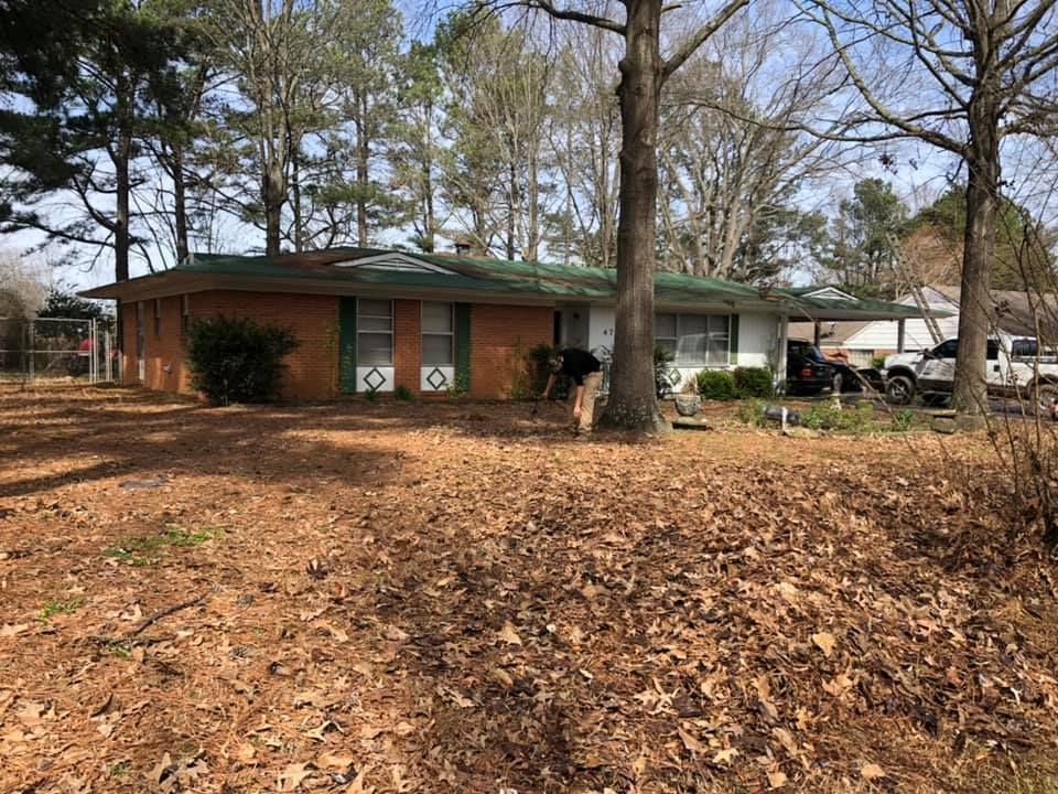 Red brick ranch house with green roof and brown leaf-covered yard.