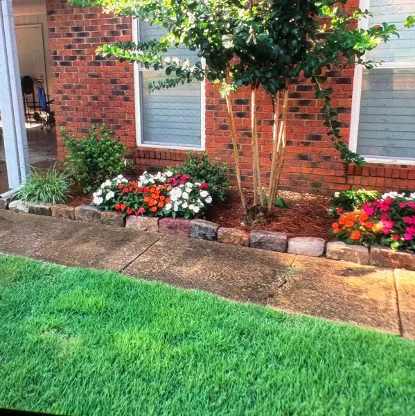 Brick building with a landscaped garden featuring colorful flowers, a tree, and a green lawn.