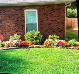 Red brick building with flowerbed of orange, pink, and white flowers in front of green grass.