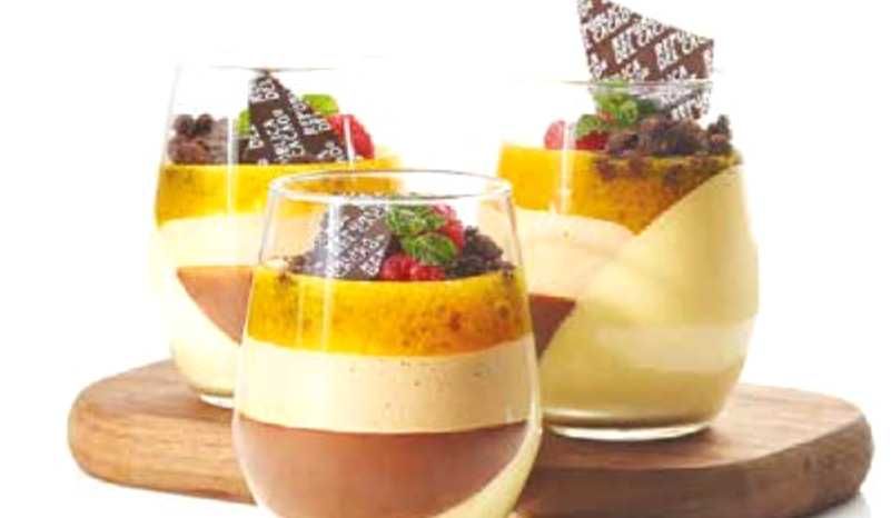 Three glasses filled with different types of desserts are sitting on a wooden cutting board.