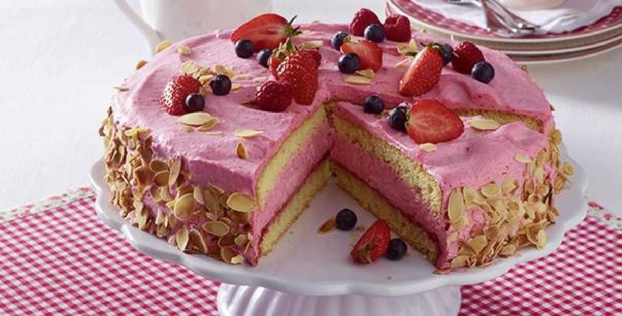 A cake with strawberries and blueberries on top of it on a cake stand.