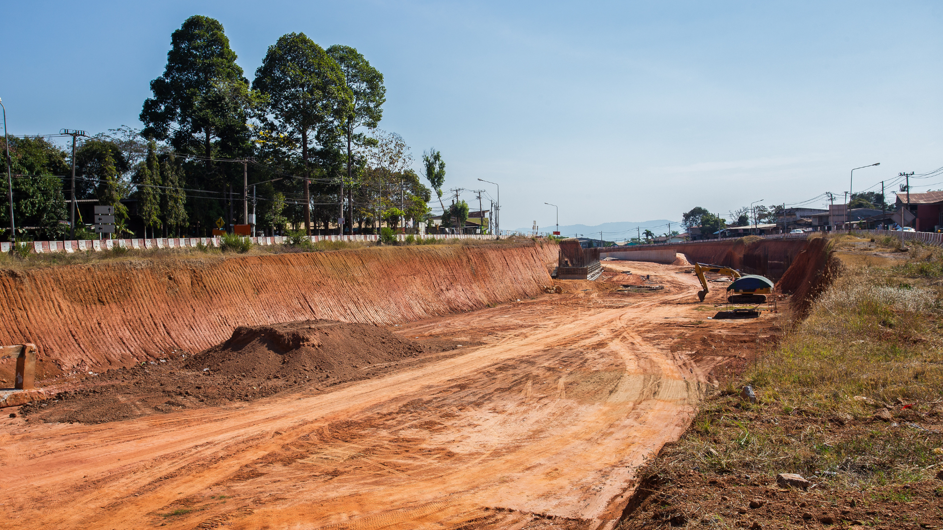 A dirt road is being built in a field with trees in the background.