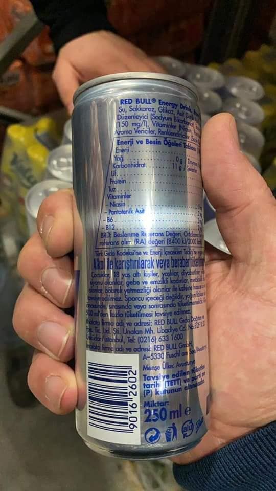 A hand holding a Red Bull energy drink can, with nutritional information visible in blue and white text.