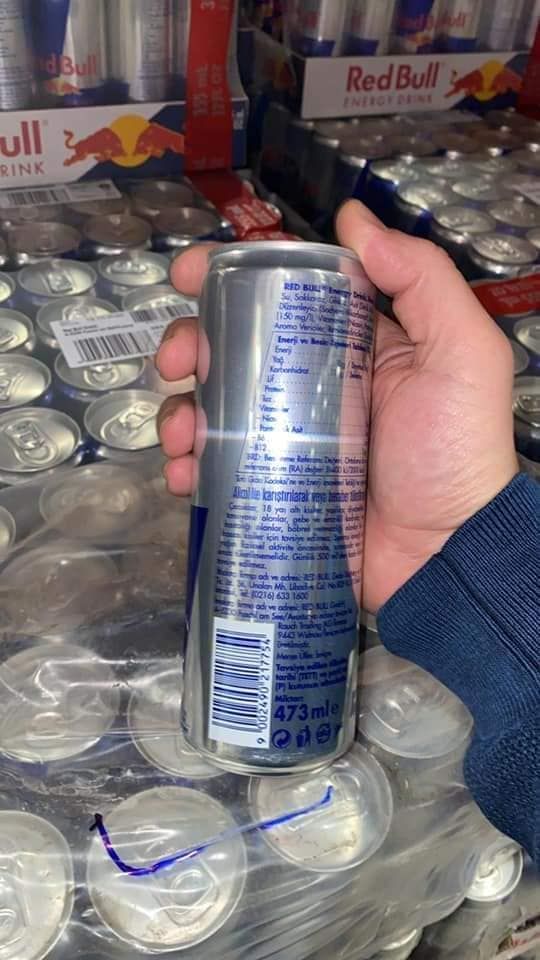 Hand holding a Red Bull energy drink can; multiple cans in the background.